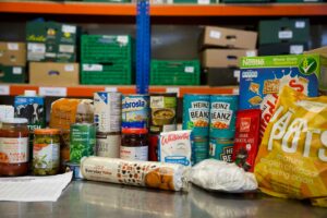 a selection of food stacked up from an emergency food parcel, tined and packaged foods such as beans and biscuits